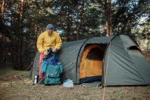 Man in Yellow Jacket and Blue Pants Standing Near Orange and Gray Dome Tent